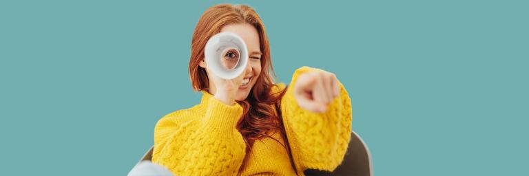 Bild zeigt eine Frau die durch eine Papierrolle schaut