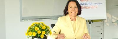 Monika Junginger am Tisch mit Blumen und Arbeitsblock bei MM-Empowerment
